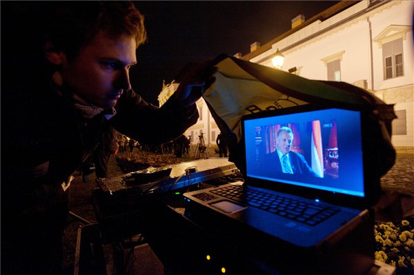 Egy demonstráló a laptopján nézi Schmitt Pál televíziós interjúját, amelyet a közmédiának adott.  A Sándor-palota előtt egyszerre vannak jelen a Schmitt Pál mellett és ellen demonstrálók csoportjai. MTI Fotó: Koszticsák Szilárd