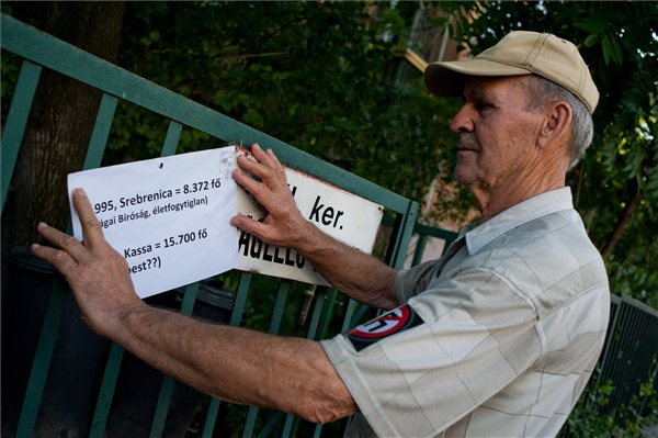 Budapest, 2012. július 16. - Gresa Lajos holokauszt túlélő egy figyelemfelkeltő táblát ragaszt az utcanévtáblára, a Simon Wiesenthal Központ által háborús bűnösként számontartott egykori katonatiszt, Csatáry László feltételezett lakhelyéül szolgáló épülete előtt a budapesti Jagelló utcában, ahol az EUJS aktivistái és önkéntesi követelik, hogy a rendőrség mielőbb tartóztassa le a 97 éves Csatáry Lászlót, aki a The Sun című brit lap szerint 15.700 zsidó auschwitzi deportálásában működött közre. MTI Fotó: Kallos Bea