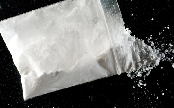 BHKNH7 image of bag of cocaine powder spilling out onto black mirror