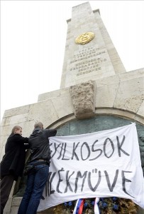 Incze Béla, a Hatvannégy Vármegye Ifjúsági Mozgalom (HVIM) alelnöke (b2) és Barcsa-Turner Gábor társelnök "Gyilkosok emlékműve" feliratú transzparenst helyez el a szovjet hősi emlékműnél a belvárosi Szabadság téren 2014. április 24-én, ahol sajtótájékoztatót tartottak a német megszállás áldozatainak tervezett emlékművével kapcsolatban. MTI Fotó: Kovács Tamás