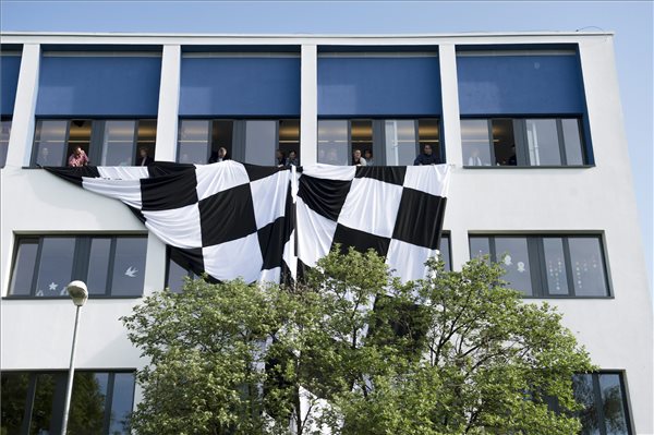 Pedagógusok egy nagyméretű kockás zászlót engednek le a Budaörsi Herman Ottó Általános Iskola ablakaiból