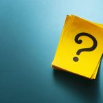 Stack of bright colorful yellow cards with question mark viewed from above on a blue background with copy space